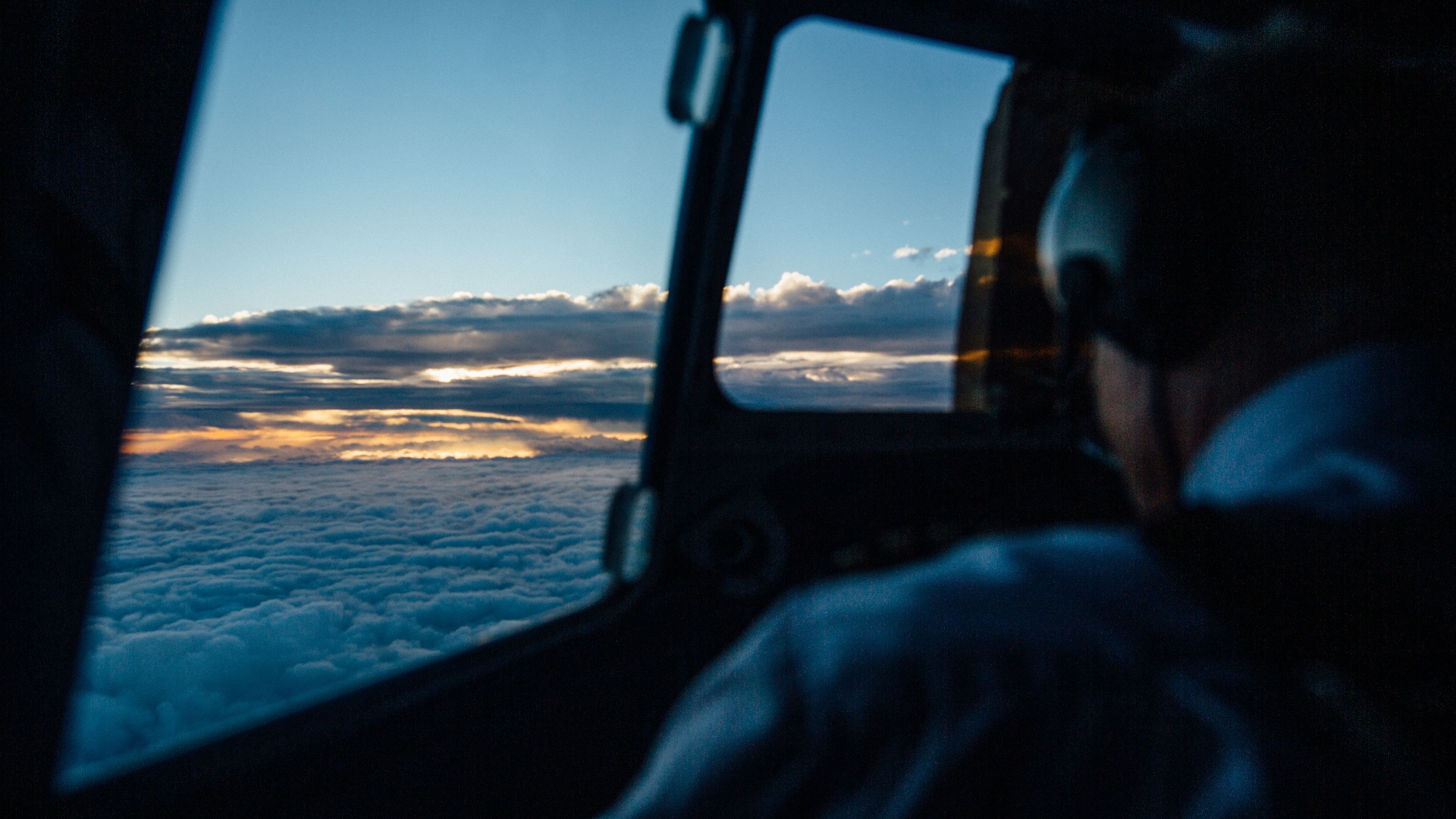 Golden sunset above the clouds seen from the cockpit window of a small aircraft.