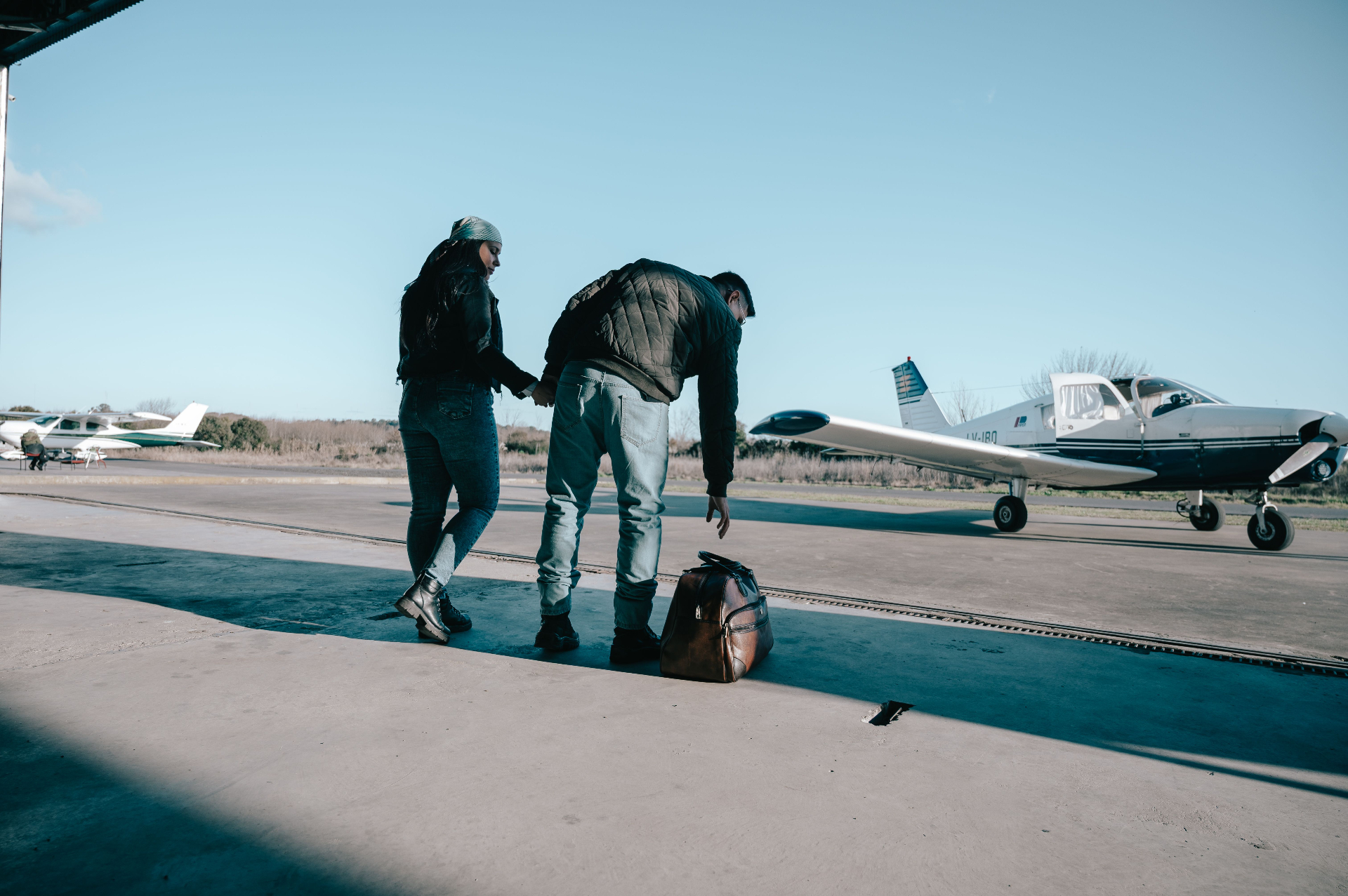 A couple pausing beside a packed bag at the hangar, preparing for what comes next after treatment.