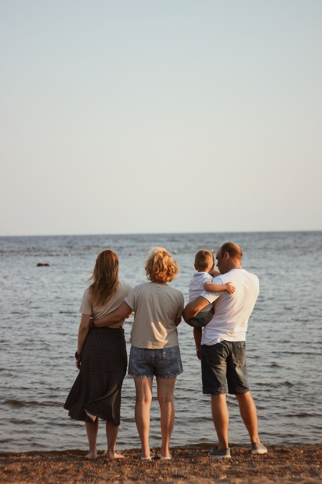 A family standing together at the shore at golden hour, looking out over the water