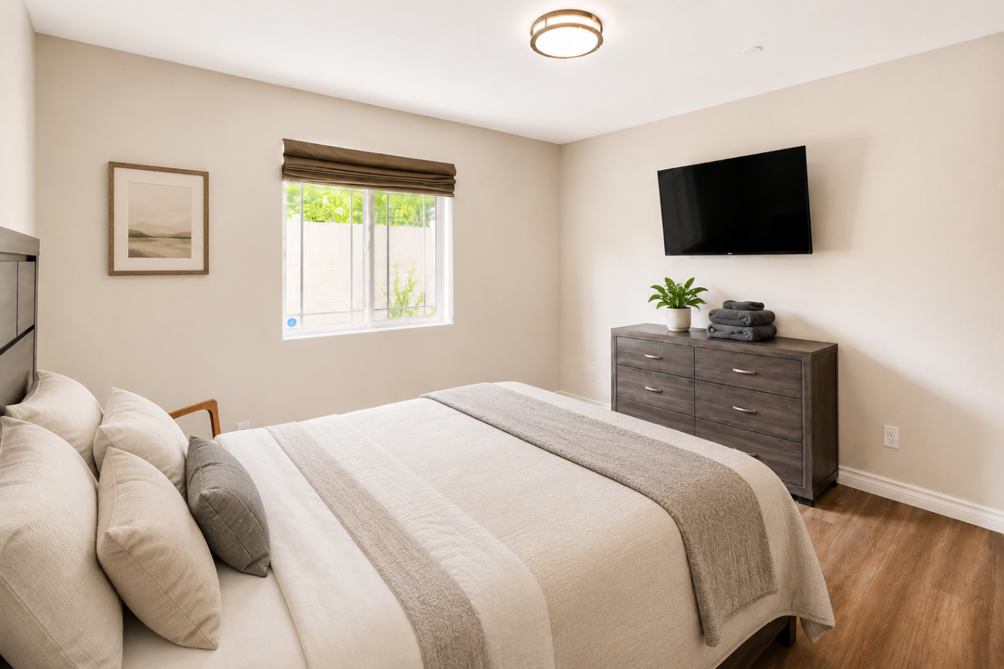 A calm private bedroom at Hangar Two with a queen bed, warm wood floors, and a wall-mounted TV