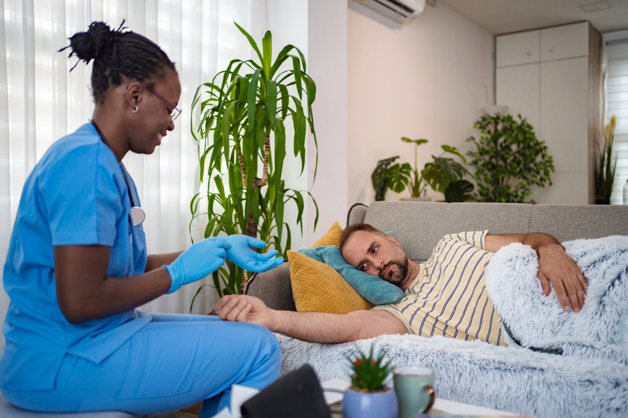 A nurse in scrubs checking on a client resting under a blanket during supervised detox
