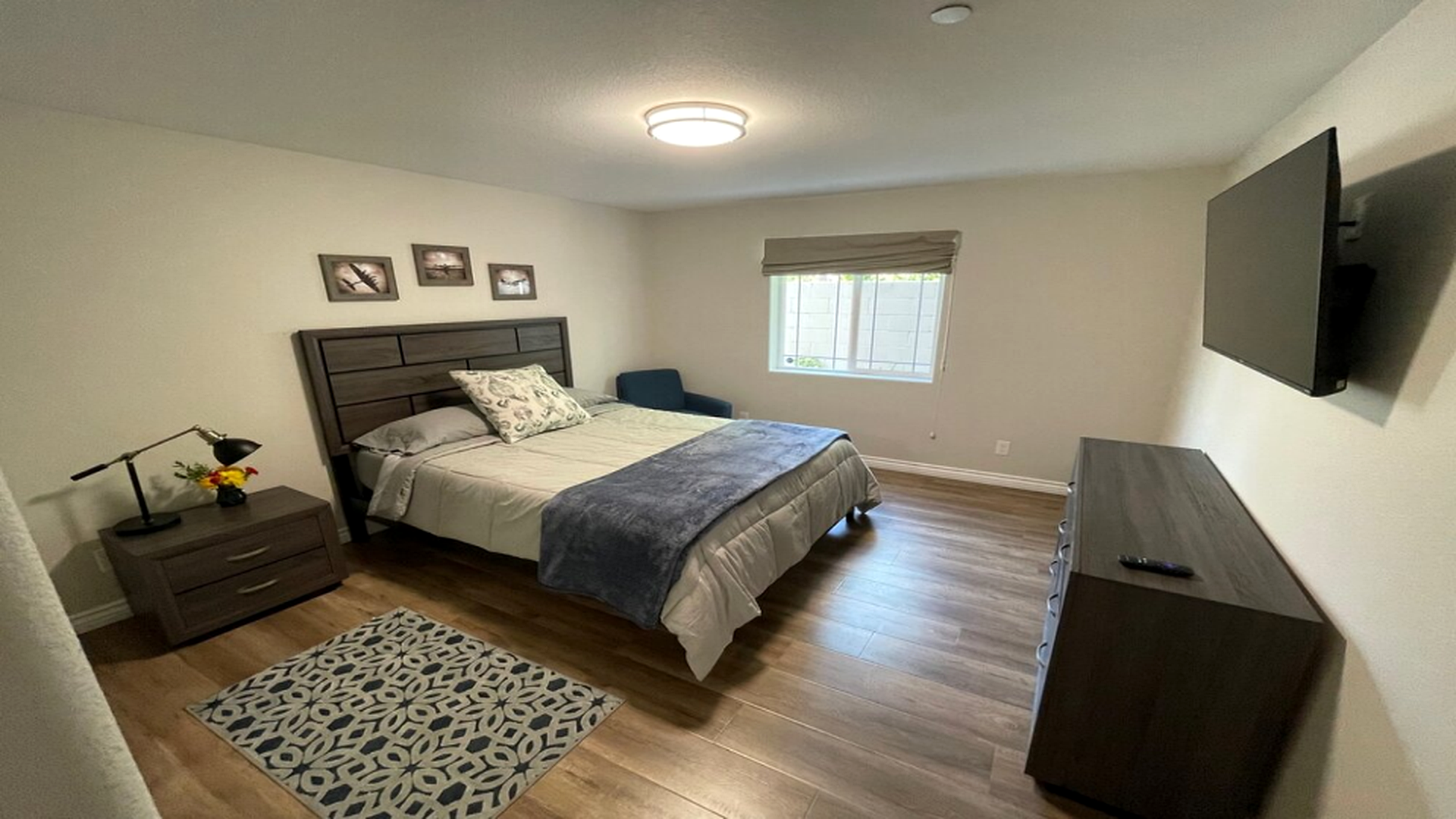 A private bedroom with a queen bed, dresser, wall-mounted TV, and framed aviation prints