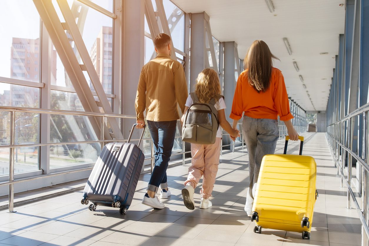 A family walking together through a sunlit airport terminal with their luggage