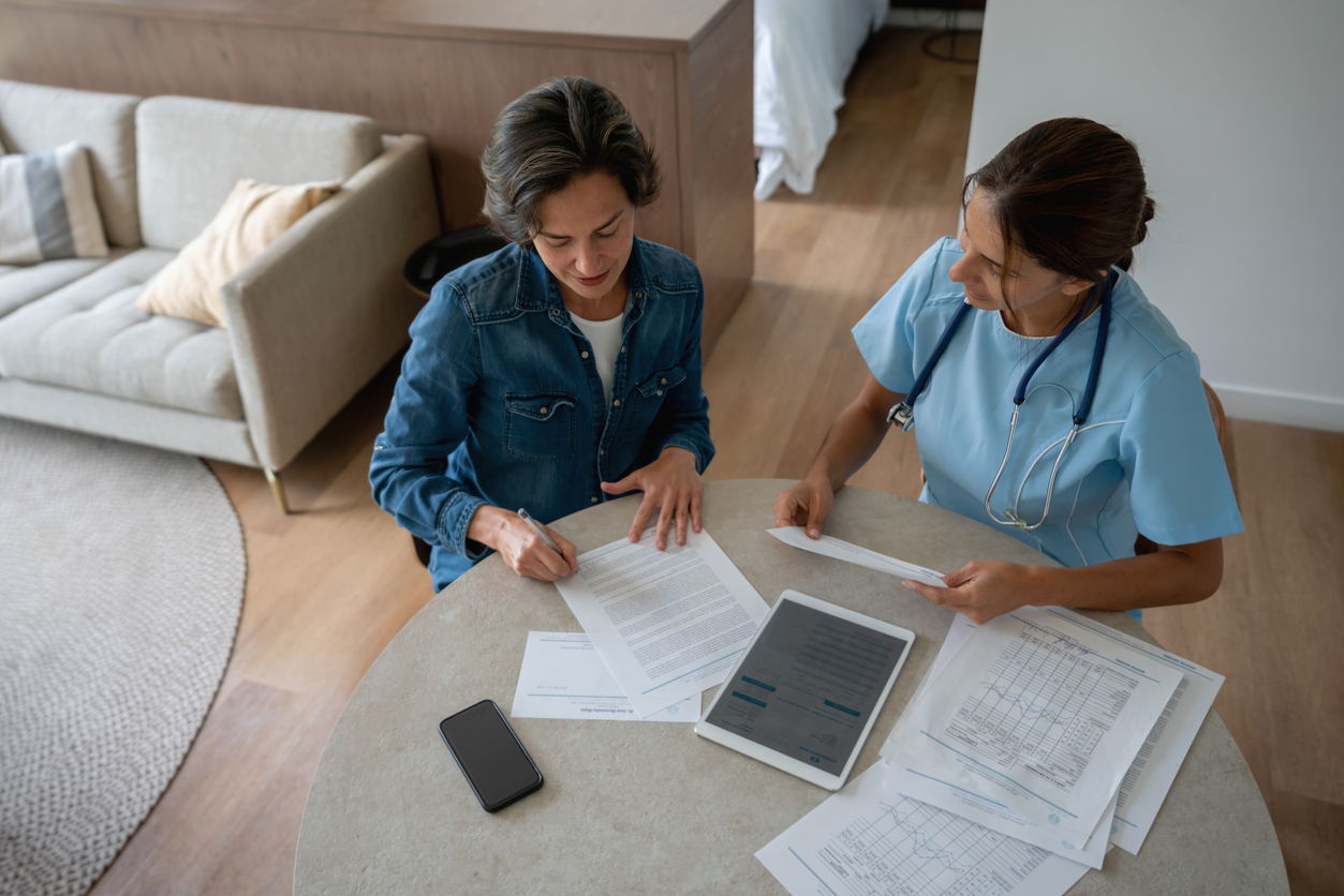 A nurse and a client sitting at a table going through benefits paperwork together