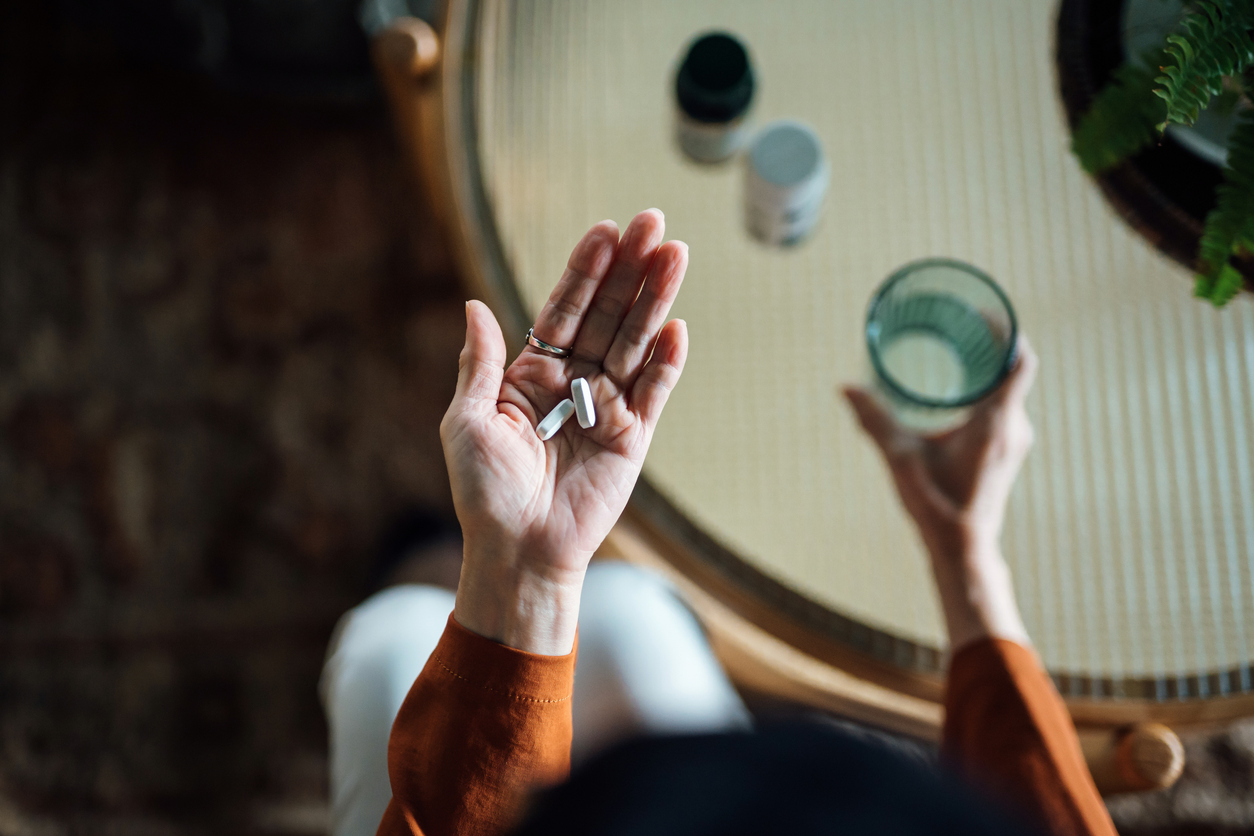 Prescription medication in a person's hand with a glass of water nearby